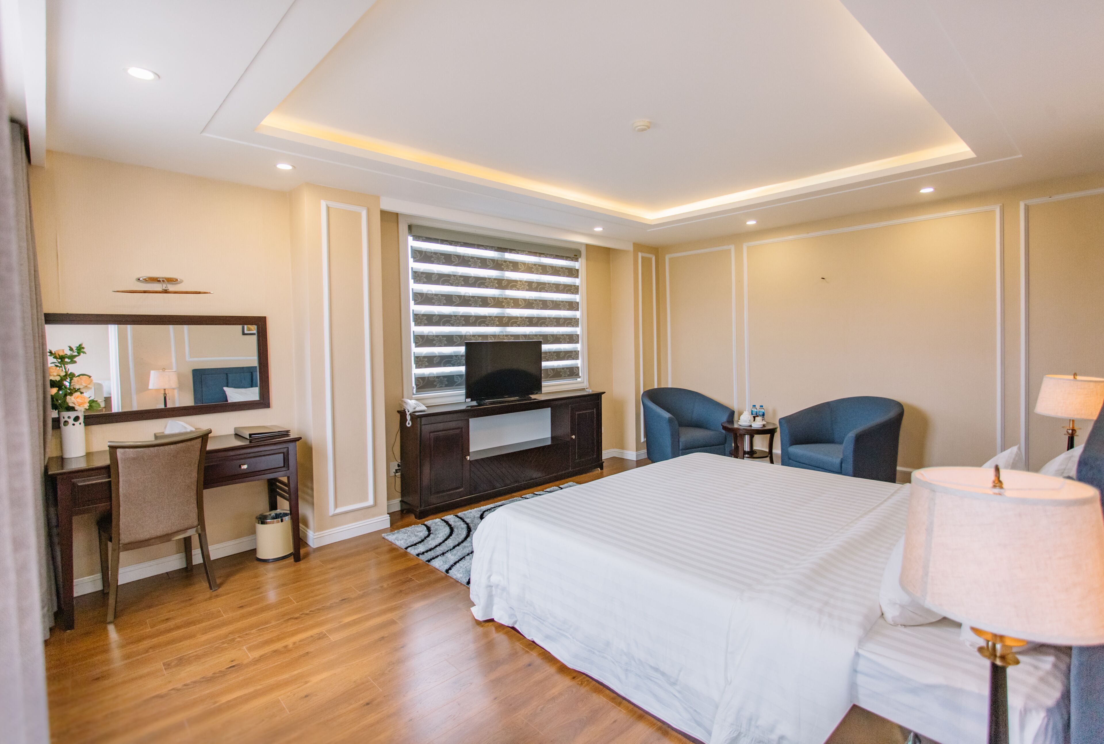 A hotel room with a large bed, a desk with a chair, a television, and two armchairs.
