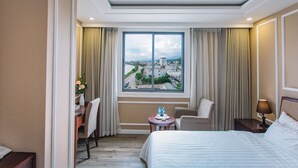A hotel room with a large window, a bed, a desk, a chair, and a small table with a lamp. - Cao Minh Hotel Lao Cai (Lao Cai)