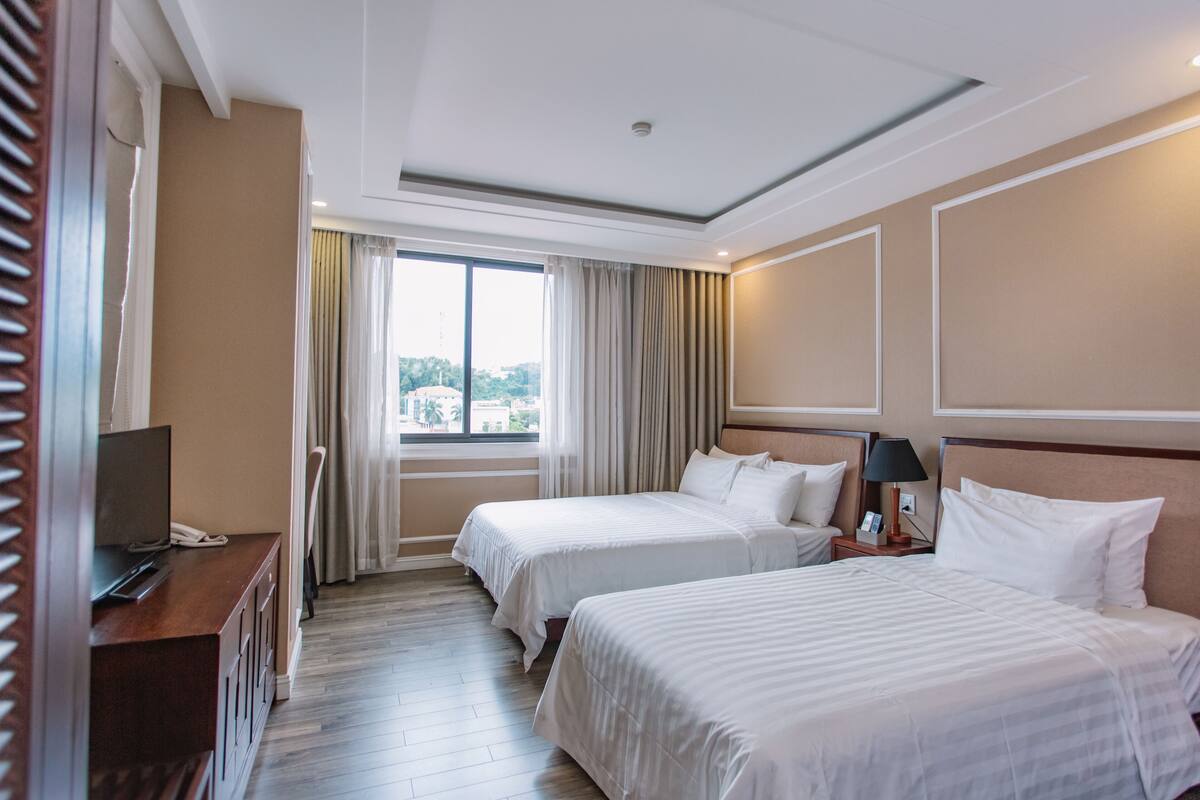Habitación de hotel con dos camas, televisión, escritorio y ventana con cortinas.