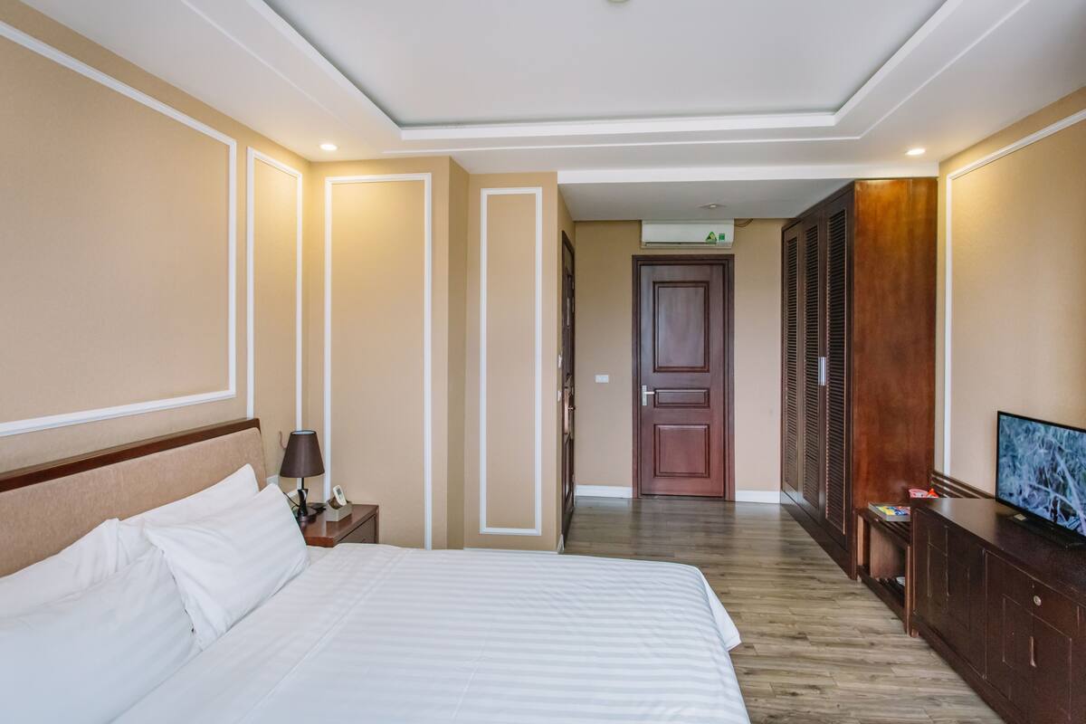 Habitación de hotel con una cama grande, un televisor, un aparador de madera y una puerta que da a otra habitación.