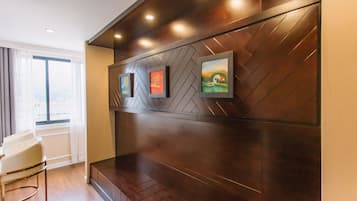 A modern hotel lobby with a wooden herringbone wall, framed artwork, and a seating area with a chair.