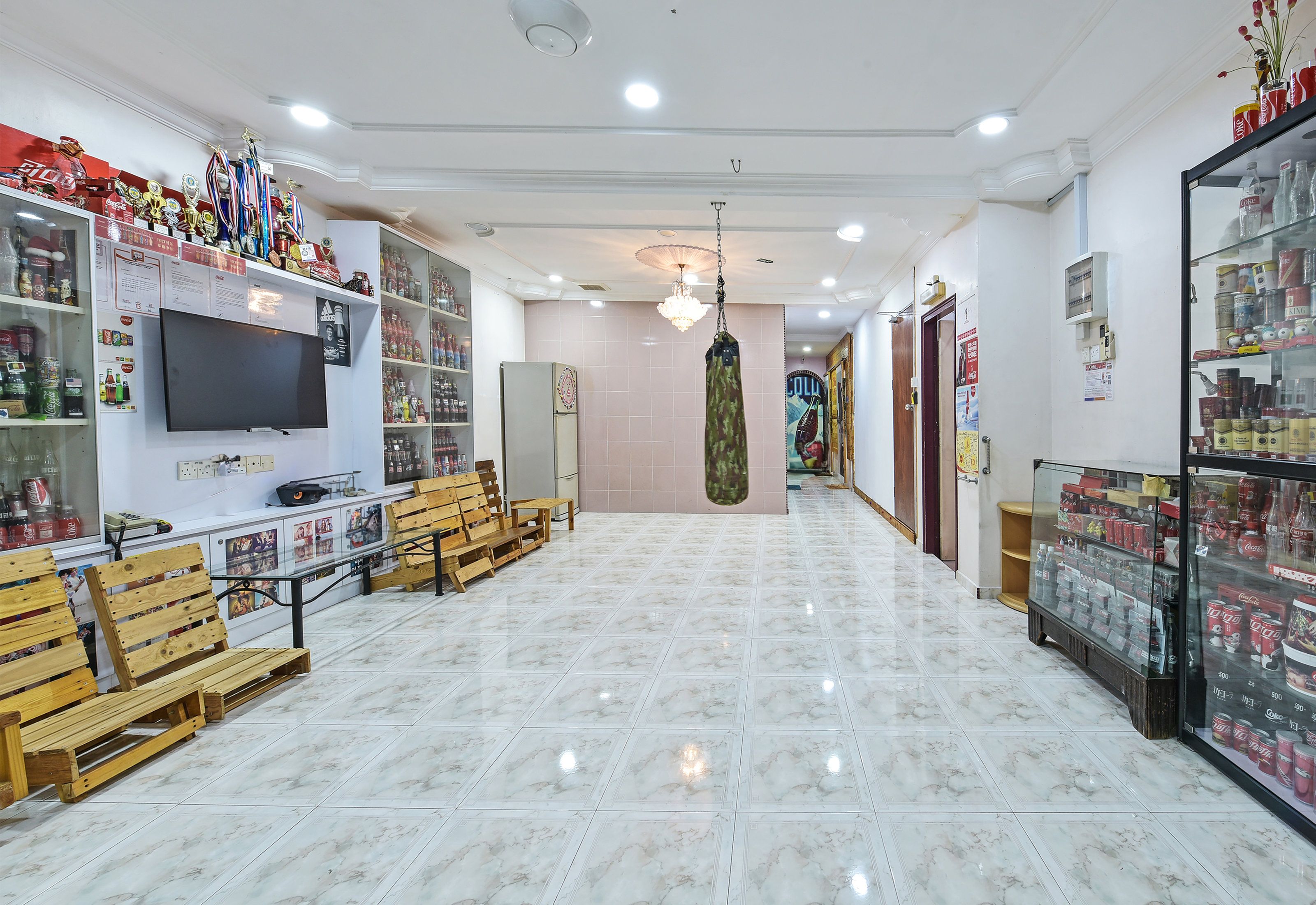 A spacious hallway with a flat-screen TV, wooden benches, and shelves stocked with various items.
