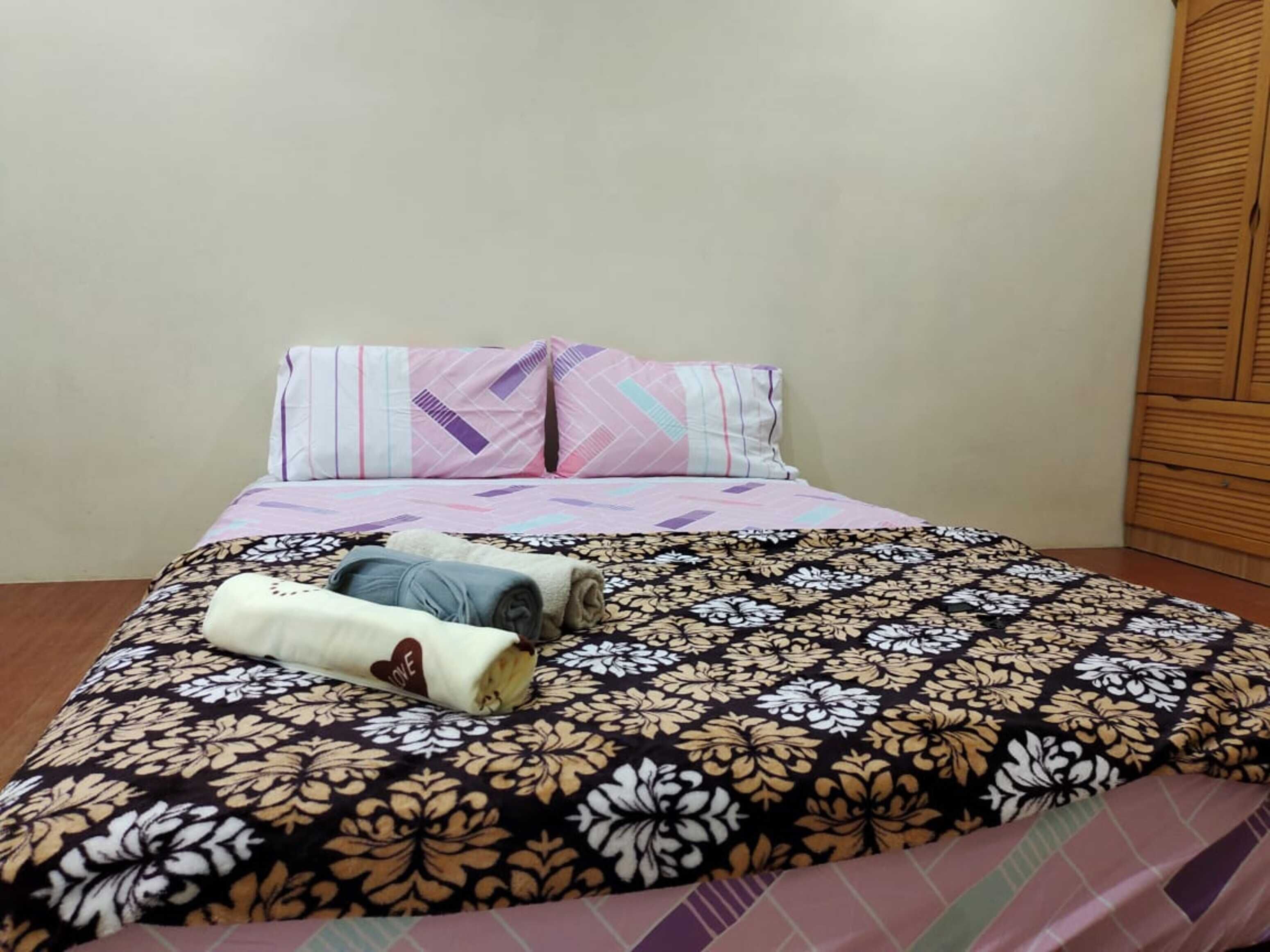 Un lit recouvert d’une couvre-lit à motifs floraux, deux oreillers aux motifs géométriques et des serviettes enroulées posées sur le lit.
