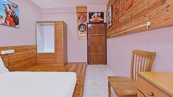 A bedroom with a bed, a wooden wardrobe, a desk, and a chair. There are posters on the wall and a door with a handle.