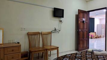 Un dormitorio con cama, dos sillas de madera, cómoda, televisor montado en la pared y una puerta abierta que da a otra habitación.