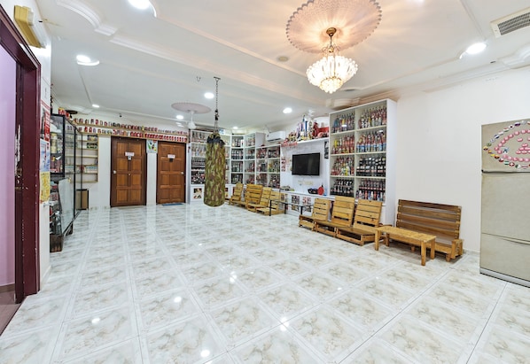 A spacious room with a marble floor, wooden benches, a television, and shelves stocked with various items.