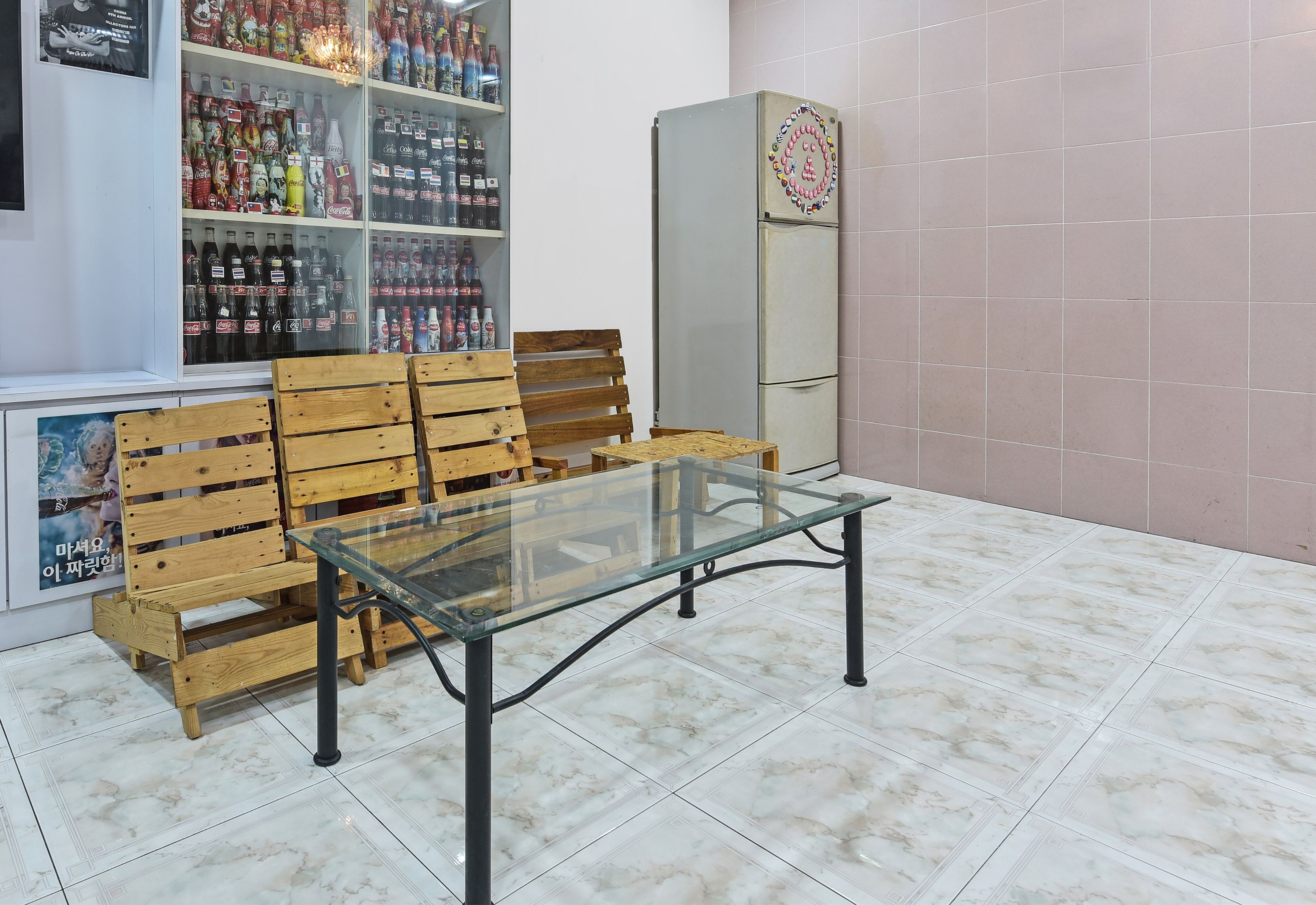 A room with a glass-top table, wooden benches, and shelves with various bottles.