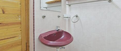 Een badkamer met een houten deur, een rode wastafel, een spiegel, een handdoekhouder en een plankje.