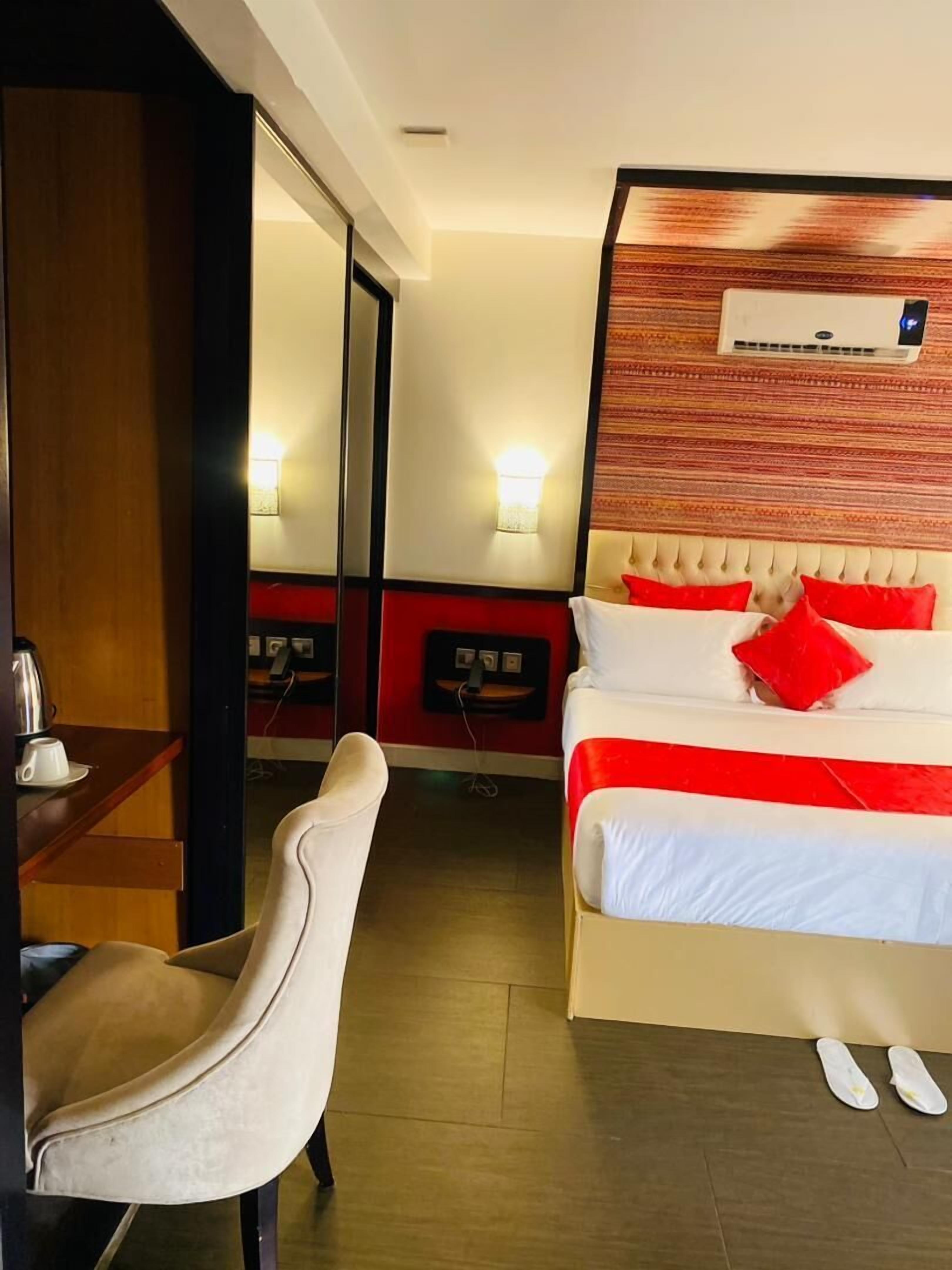 Una habitación de hotel con cama, una silla, una mesita de noche y un equipo de aire acondicionado.