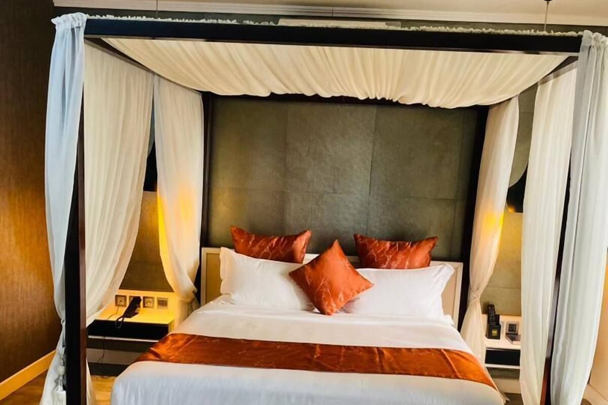 A large bed with a canopy, white bedding, and orange pillows.