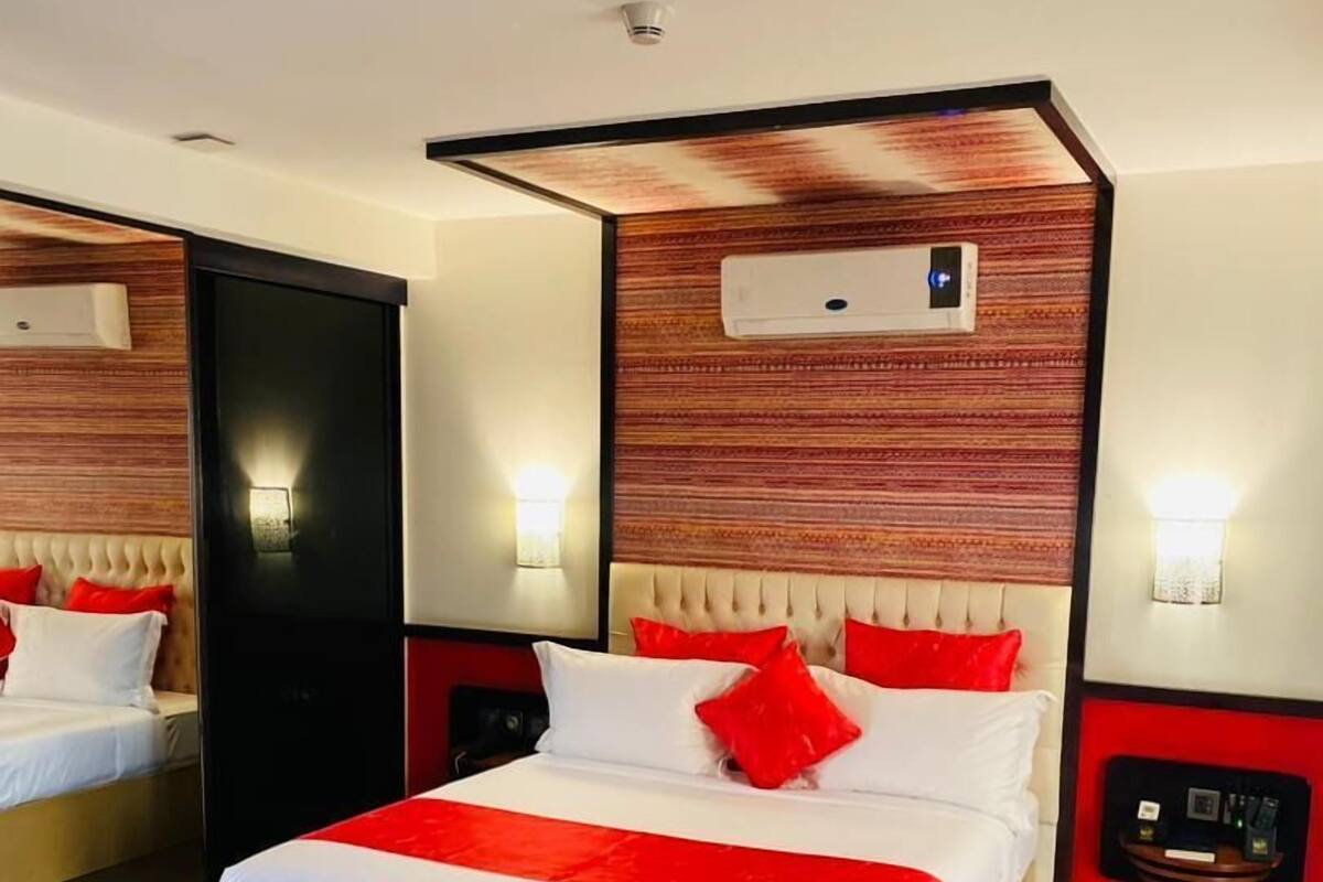 A hotel room with a large bed, two bedside tables, a mirror, and a wall-mounted air conditioning unit.