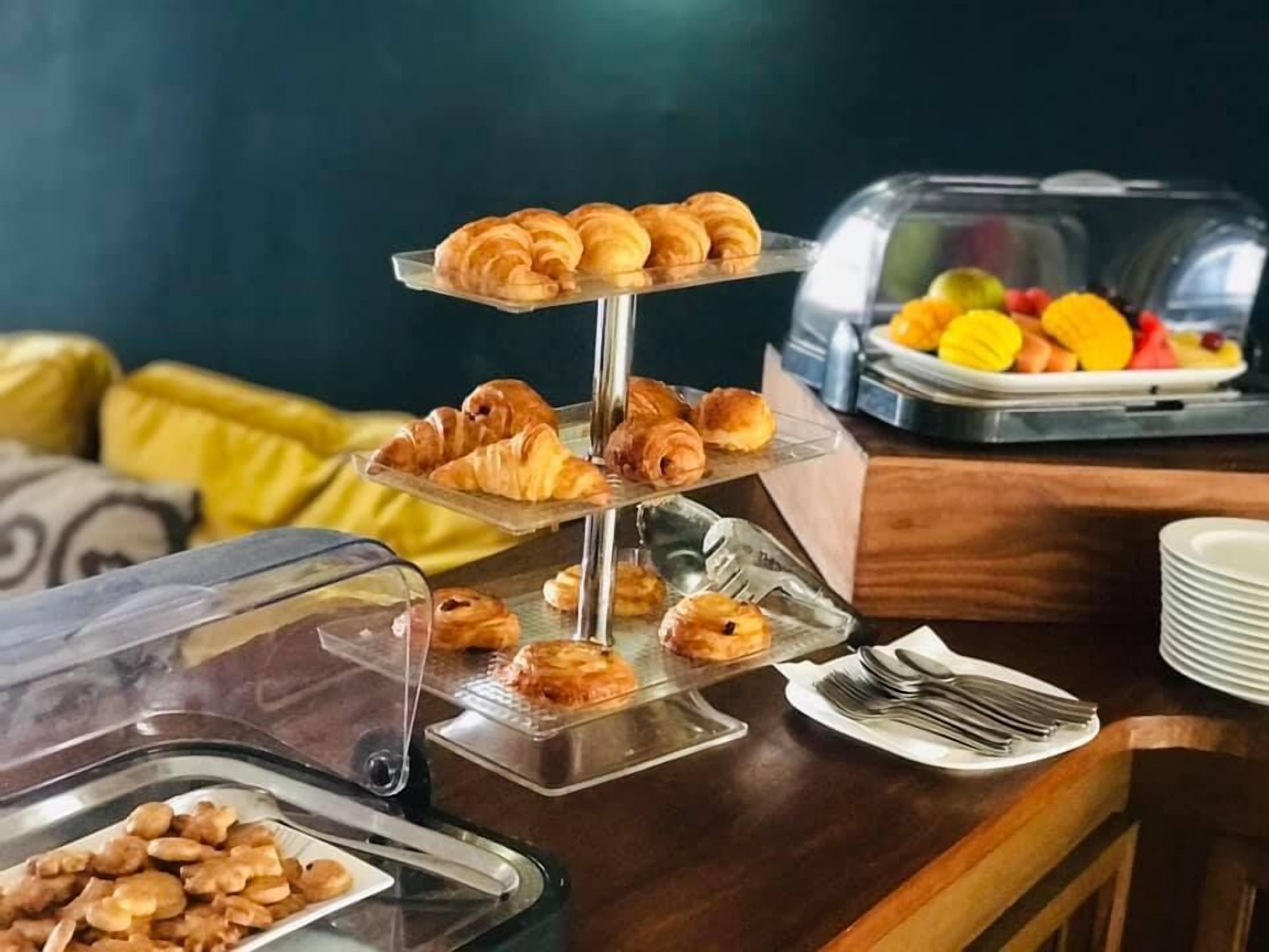 Een buffet met croissants, gebak en een fruitschaal.