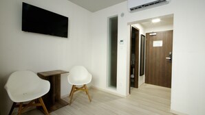 A room with a flat-screen TV mounted on the wall, two white chairs, a small wooden table, and a door leading to another room. - Adeba Plus (Prague)