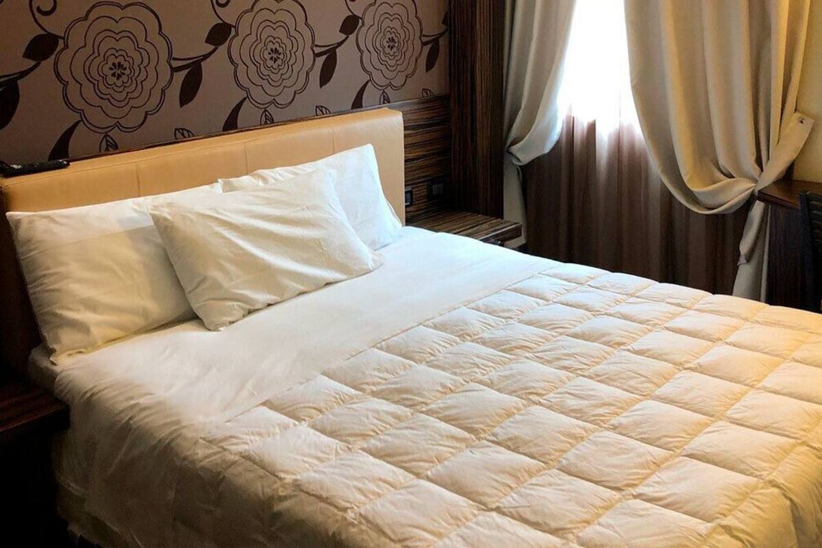 A neatly made bed with a quilted cover and two pillows, a wooden headboard, and a floral wallpaper pattern.
