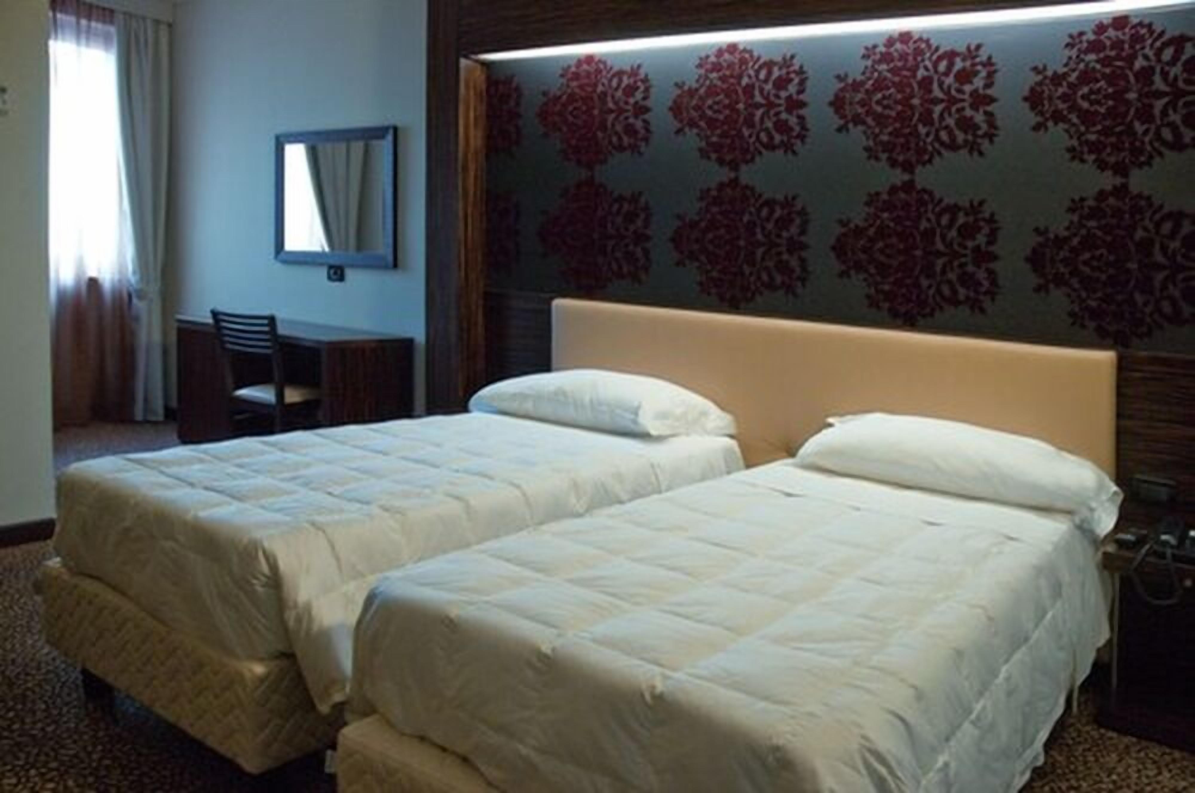 A hotel room with two beds, a desk, and a mirror.