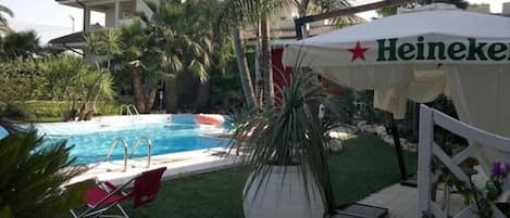 A swimming pool area with a Heineken tent, a palm tree, and a red lounge chair.