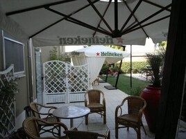 Um pátio externo com cadeiras de vime e uma mesa sob um guarda-sol com a marca Heineken.