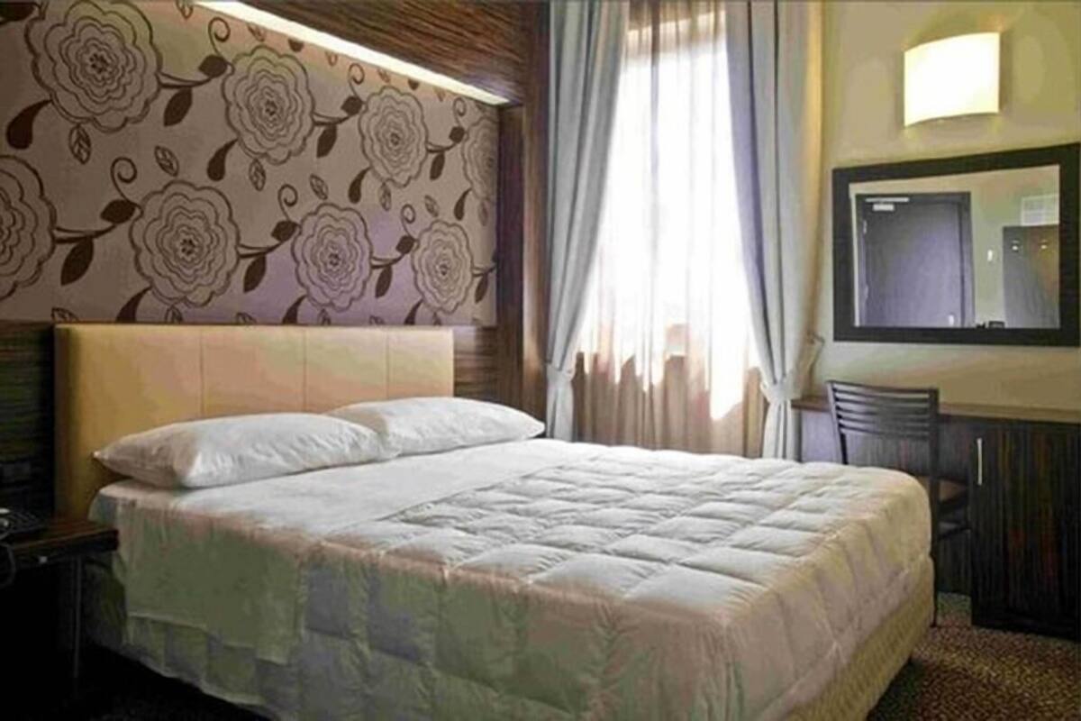 A hotel room with a large bed, a desk with a chair, a mirror, and a window with curtains.