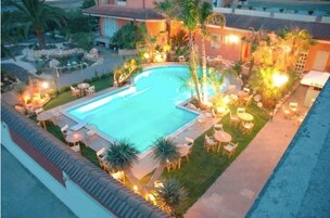 Piscina cercada por assentos ao ar livre e palmeiras, com um edifício ao fundo.