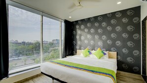Un dormitorio con un ventanal grande, una cama con colcha de colores y una pared negra con un diseño de remolinos.