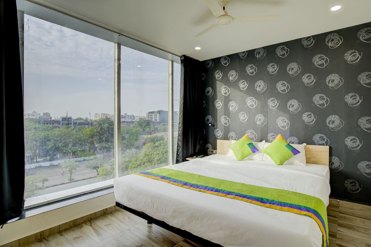 A bedroom with a large window, a bed with a colorful bedspread, and a black wall with a swirl pattern.