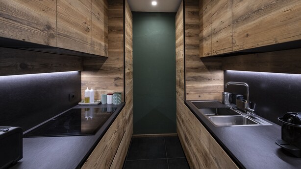 A modern kitchen with wooden cabinets, a black countertop, and a green accent wall.