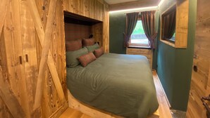 A cozy room with a bed, wooden walls, and a window with curtains.