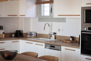 A modern kitchen with white cabinets, a stainless steel sink, a dishwasher, and a microwave. - Villa Lefko a Cycladic escape in the heart of the Aegean (Μέγας Γιαλός)