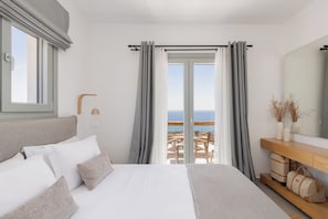A bedroom with a bed, a bedside table, a mirror, and a view of the sea. - Villa Lefko a Cycladic escape in the heart of the Aegean (Μέγας Γιαλός)
