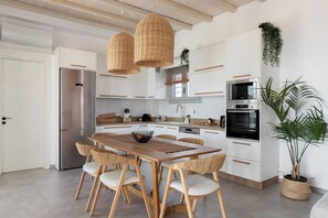 Eine moderne Küche mit weißen Schränken, Edelstahlgeräten, einem Holzespeisetisch mit Korbstühlen und hängenden Korbstühlen.