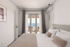 Ein Schlafzimmer mit einem großen Bett, Meerblick durch eine Schiebetür und einer unter der Decke montierten Klimaanlage.