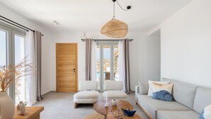 En moderne stue med sofa, to lænestole, sofabord og et stort vindue med gardiner.