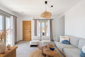 Ein modernes Wohnzimmer mit einer Couch, zwei Sesseln, einem Couchtisch und einem großen Fenster mit Vorhängen.