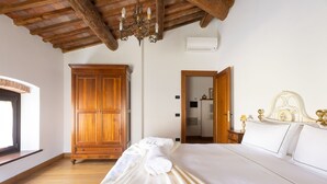 Een slaapkamer met een houten garderobe, een bed met witte lakens en een kroonluchter.