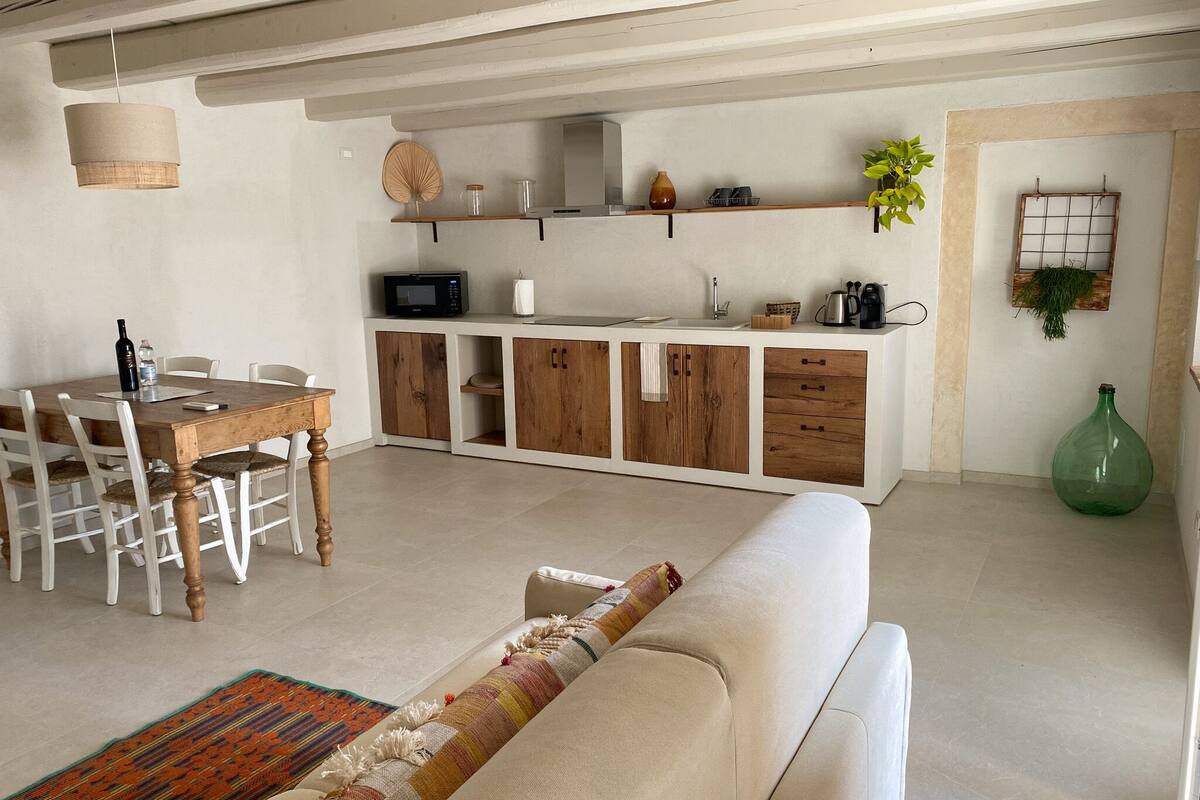A modern kitchen with wooden cabinets, a dining table, and a sofa in a living area.