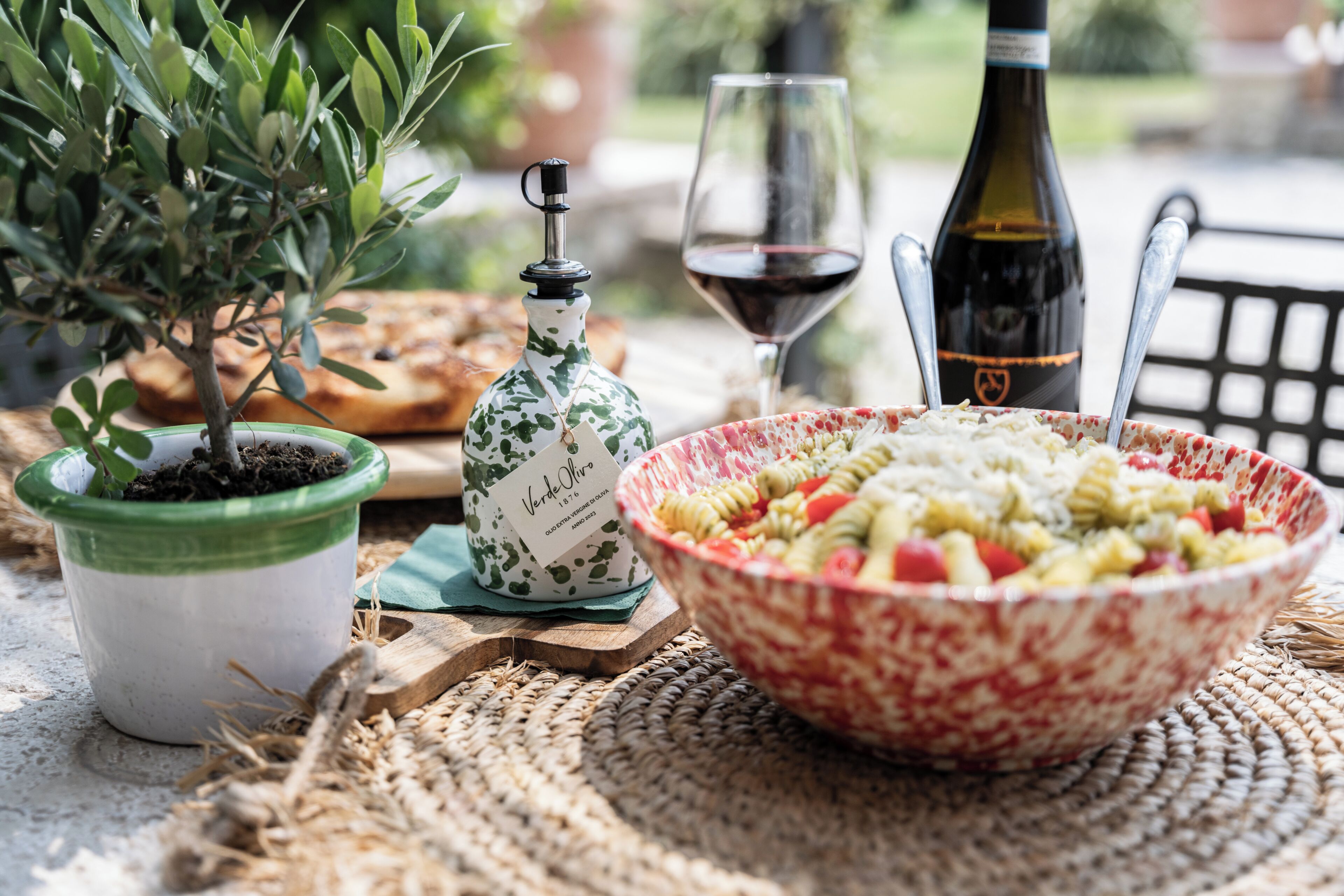 Una mesa de comedor con ensalada de pasta, una botella de vino, una copa de vino, una planta en maceta y una botella decorativa.