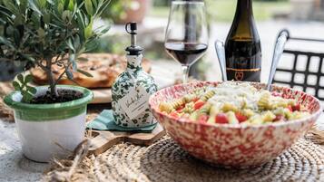 Una mesa de comedor con ensalada de pasta, una botella de vino, una copa de vino, una planta en maceta y una botella decorativa.