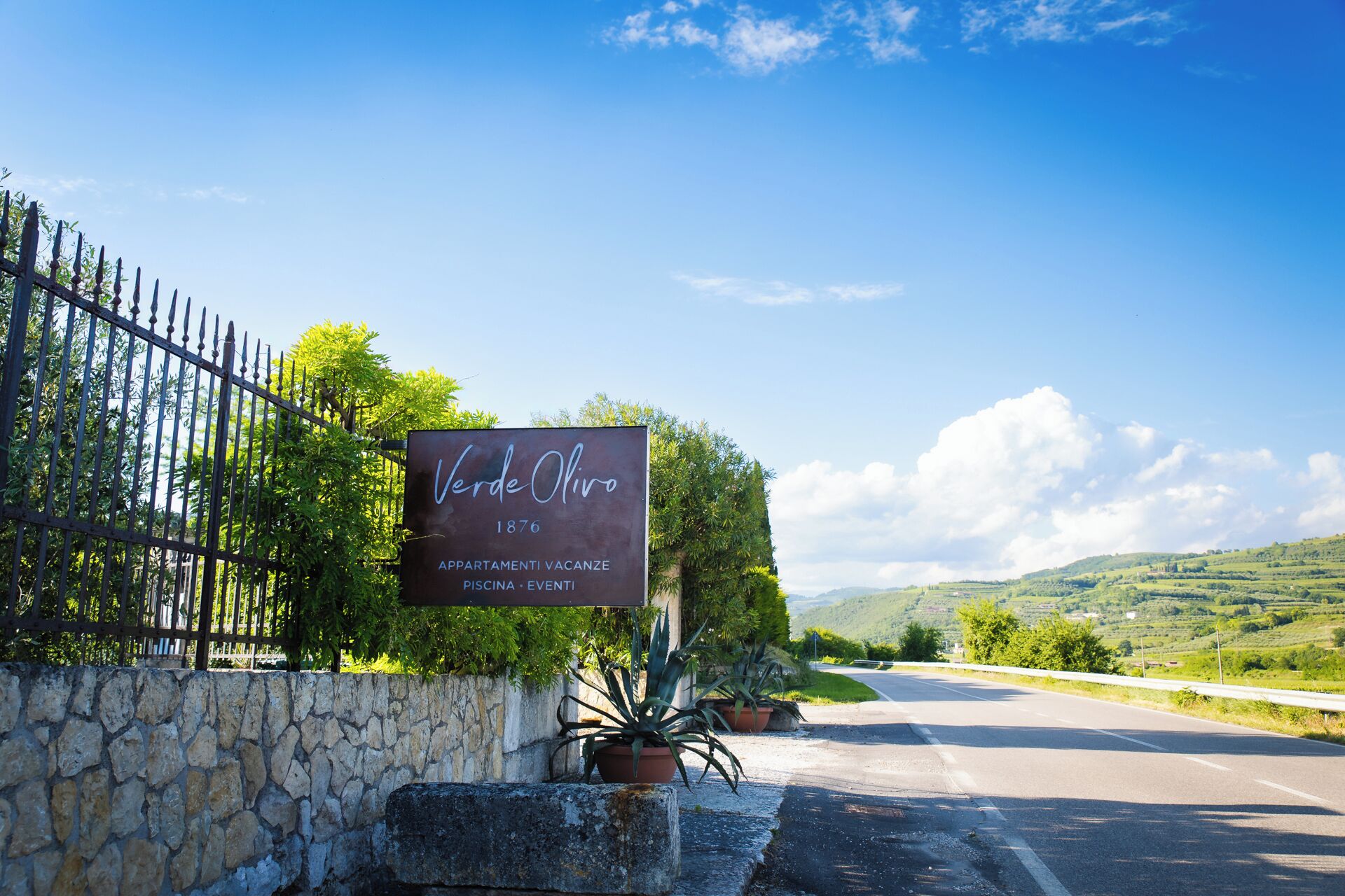 A sign for Verde Olive, established in 1876, indicating it offers apartments, a pool, and events.