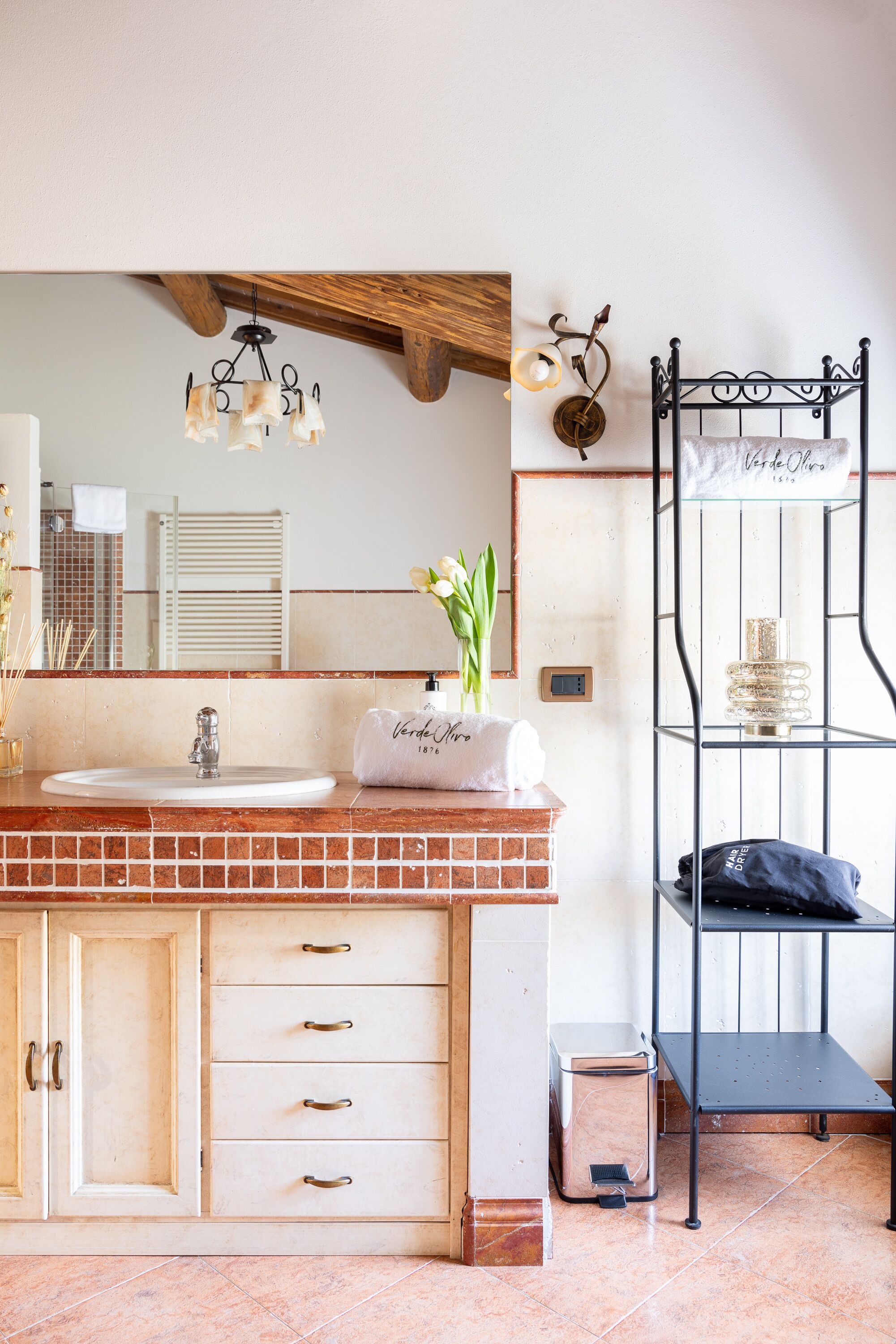 Une salle de bain avec un plafond en bois, un lavabo blanc et un miroir. On y trouve un porte-serviettes avec une serviette et un flacon de parfum.