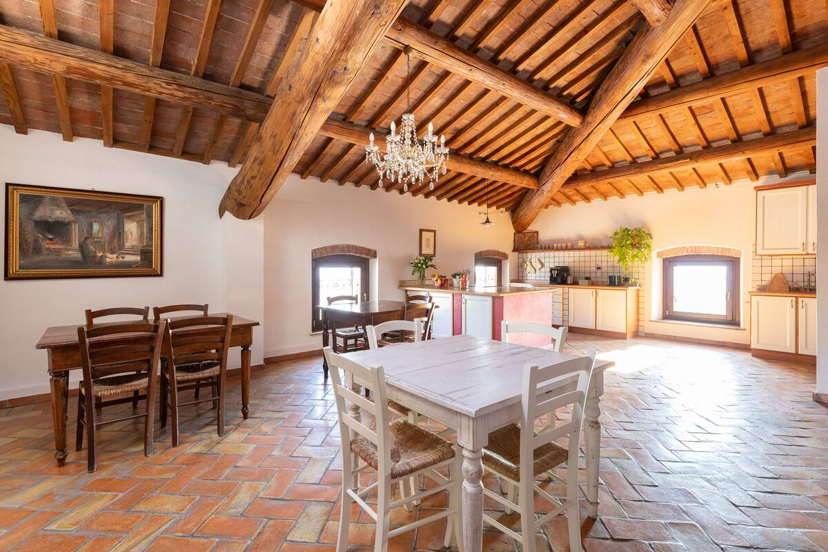 A spacious dining area with a wooden table and chairs, a chandelier, and a tiled floor.