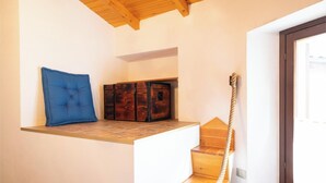 A room with a wooden ceiling, a blue cushioned bench, a wooden chest, and a spiral staircase.