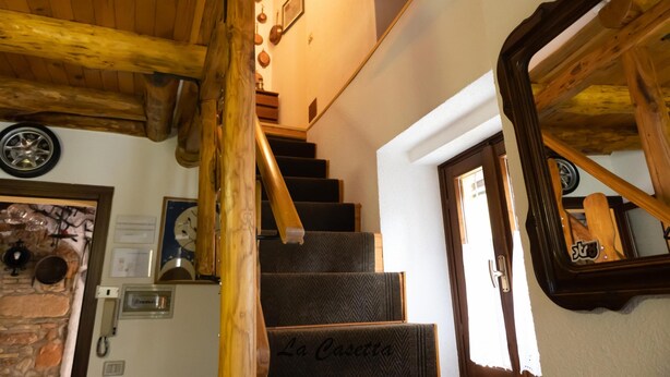 A wooden staircase with a handrail, a door with a mirror, and a wall with a clock and framed pictures.