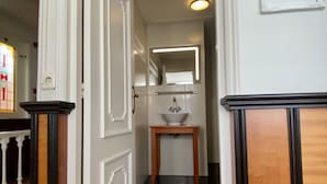 A hallway with a white door, a small table with a white sink, and a mirror above it. - Logement Garjen (Harlingen)