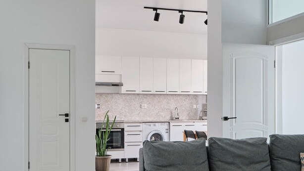 Een moderne woonkamer met een grijze bank, een eethoek met stoelen en een keuken op de achtergrond.