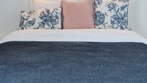 Een net opgemaakt bed met gestreepte kussens, twee ingelijste foto’s aan de muur en wandlampen voor het lezen.