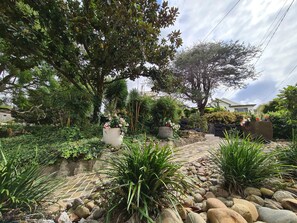 Un jardín con un sendero de piedra, diversas plantas y un gran árbol.