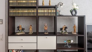 A bookshelf with multiple shelves, some with books and others with figurines. There are decorative items like a candelabra and a vase with flowers.