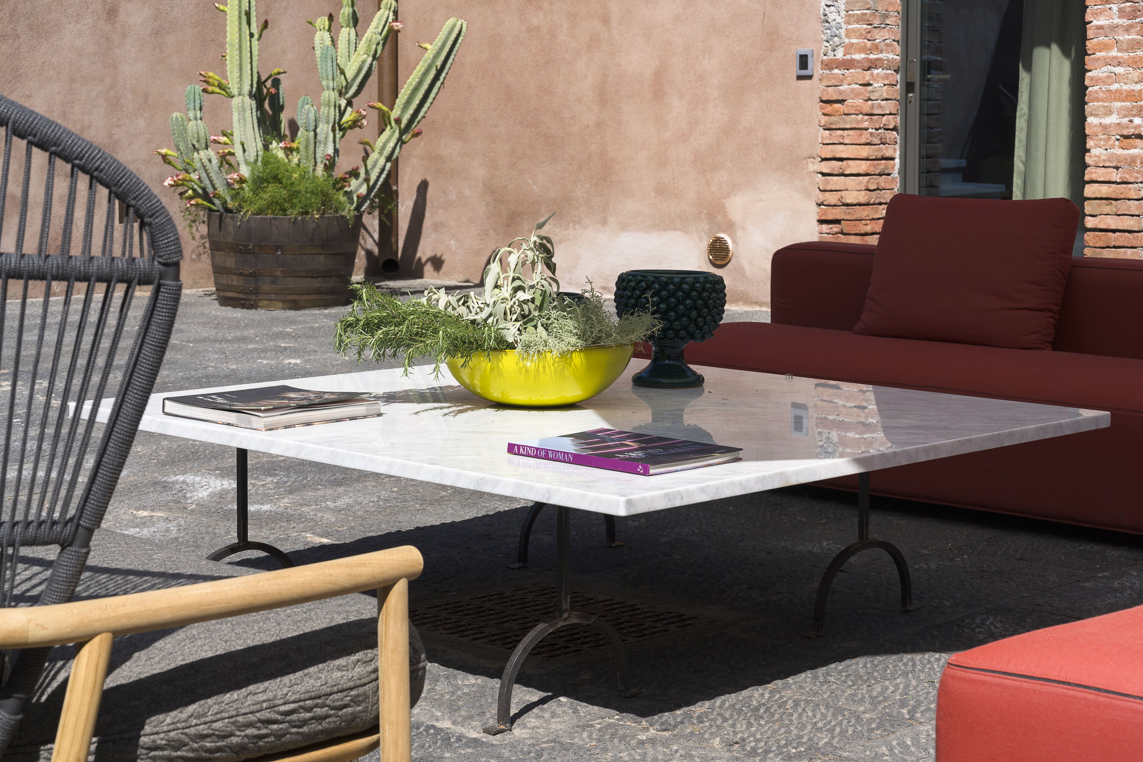 A patio with a white table, a red sofa, a yellow planter with cacti, and a black chair.