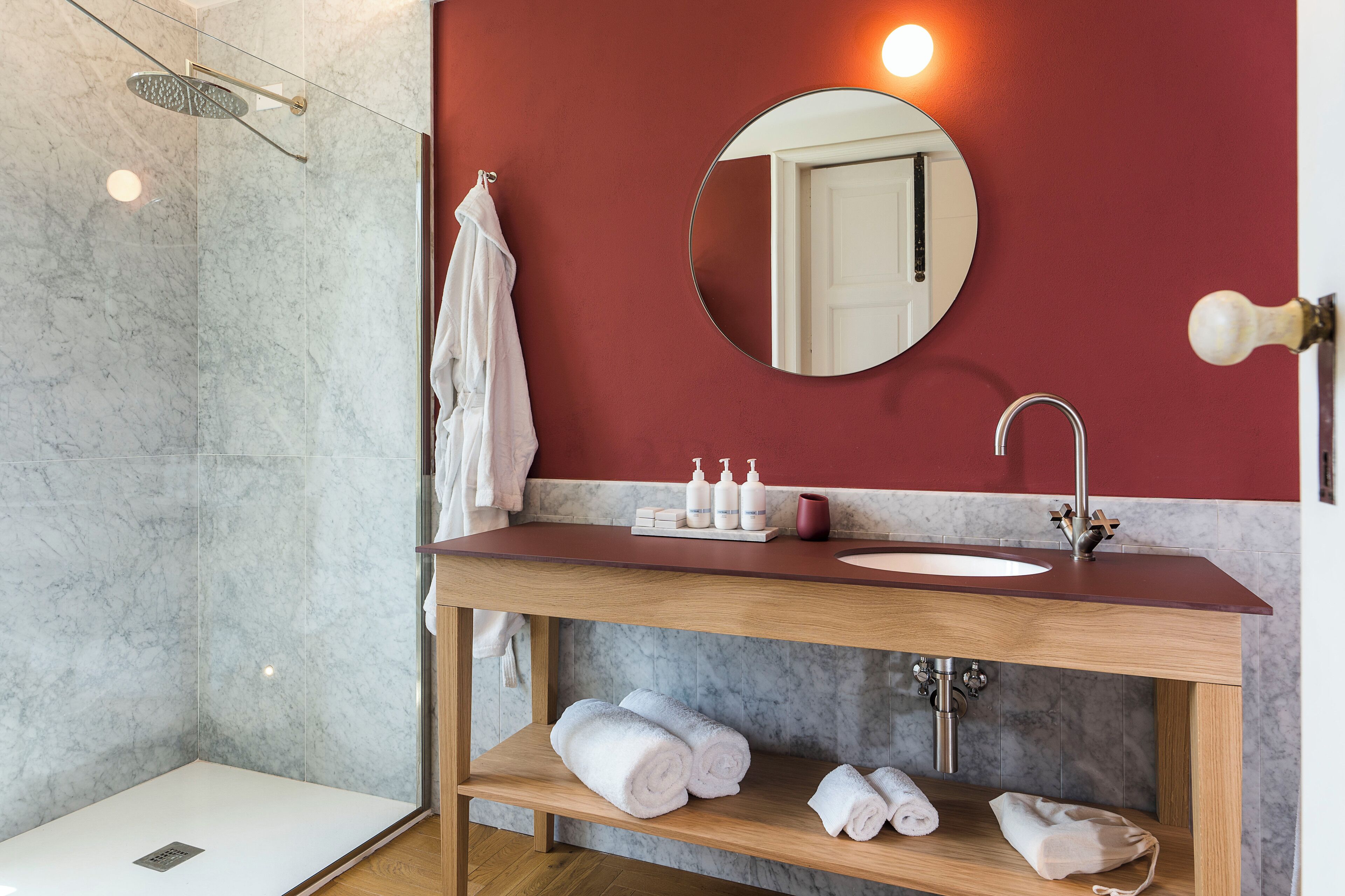 A modern bathroom with a marble shower, a wooden vanity with a sink, and a mirror.