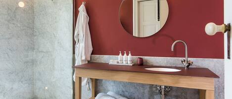 A modern bathroom with a marble shower, a wooden vanity with a sink, and a mirror.